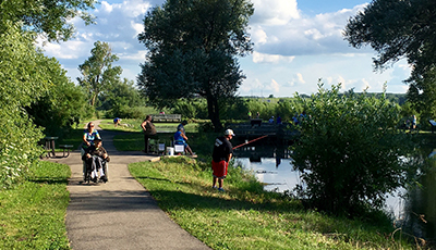 People fishing and someone in a wheelchair on the paved path by the pond